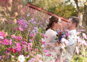 Bride and groom smiling and laughing while holding a flower bouquet and standing in the middle of a flower garden