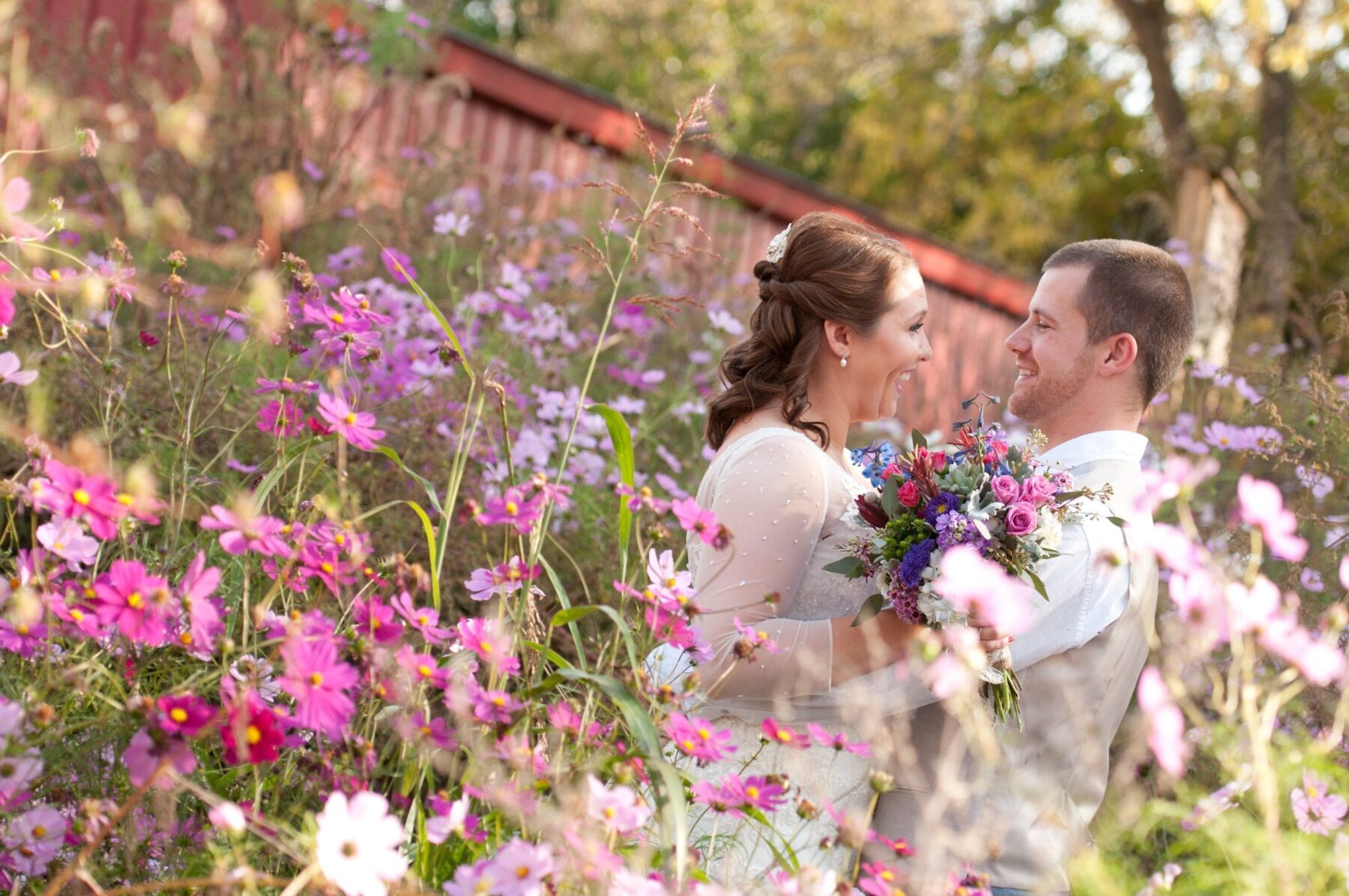 Bride and groom smiling and laughing while holding a flower bouquet and standing in the middle of a flower garden