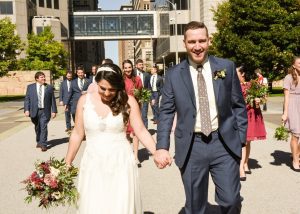 Bride and groom holding hands outside with bridesmaids and groomsmen walking behind them