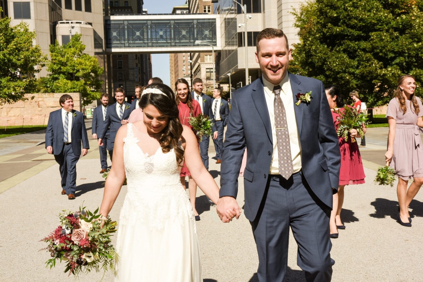 Bride and groom holding hands outside with bridesmaids and groomsmen walking behind them