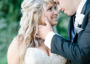 Groom holding bride while they smiling and looking into each other's eyes outside
