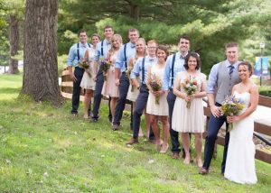 Bridesmaids holding flowers standing next to the groomsmen outside next to a tree